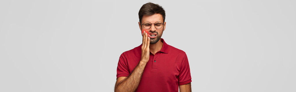 A man with glasses holding his cheek, indicating tooth or jaw pain.