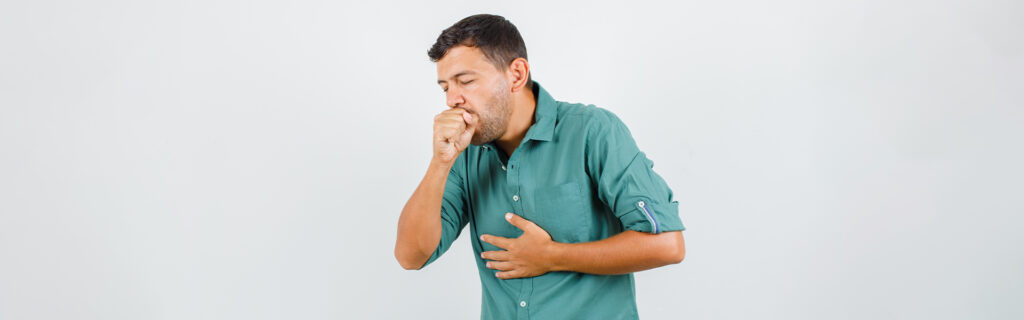 Man in a green shirt coughing into his hand, looking distressed.